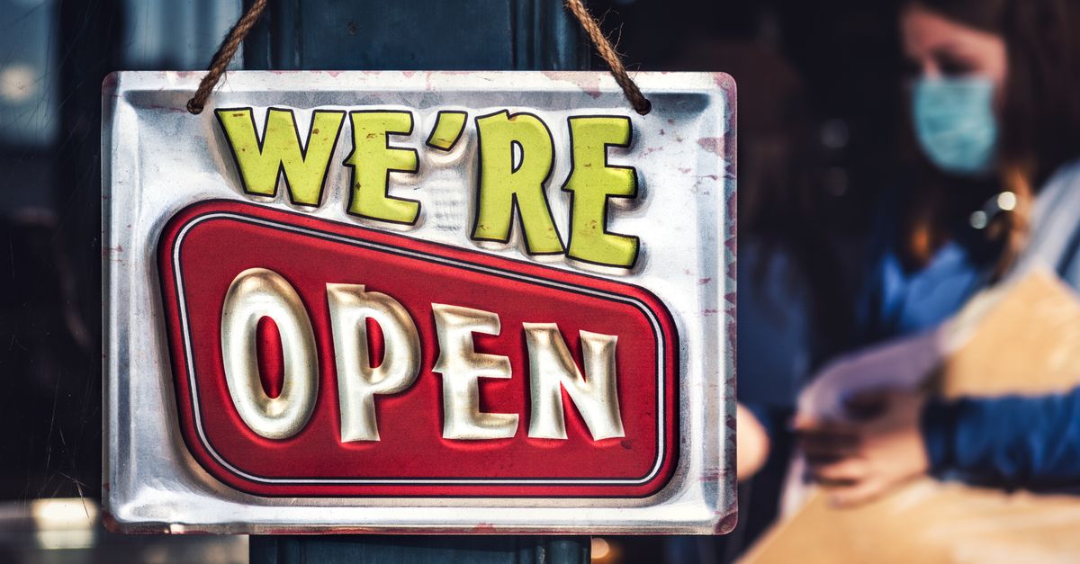 Vibrant we are open sign hanging on storefront with people in background.